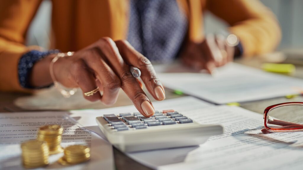 Mujer calculando impuestos con documentos y monedas sobre la mesa, ilustrando las obligaciones fiscales de emprendedores digitales en México.